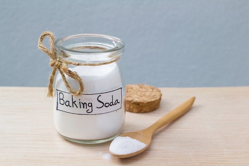 Hũ đựng bột baking soda có nắp đậy và muỗng gỗ trên bàn gỗ sáng.