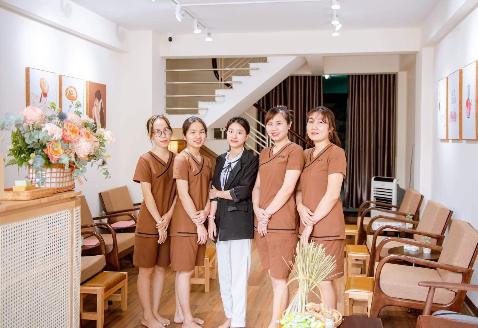 Nhóm người mặc đồng phục đứng trong không gian nội thất sáng sủa với hoa và tranh treo tường.