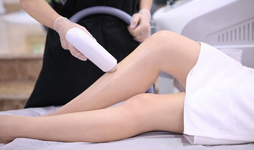 Người đang thực hiện trị liệu laser trên chân của một khách hàng trong trung tâm thẩm mỹ.