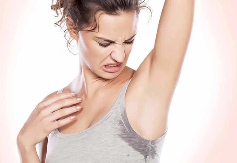 Người phụ nữ nhăn mặt nhìn áo có vết ướt dưới cánh tay, thể hiện sự khó chịu.