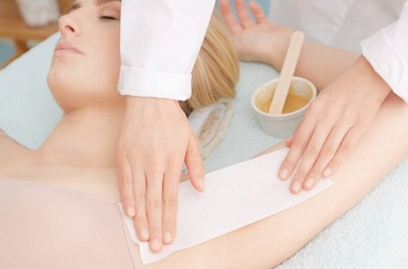 Người đang thực hiện dịch vụ tẩy lông cho khách hàng với sáp và giấy tại một spa.