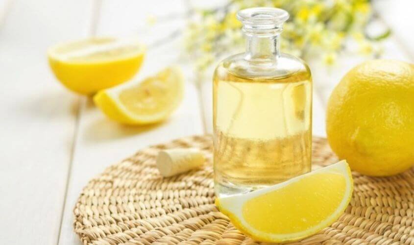 Chai dầu và lát chanh vàng trên bàn cói, chanh cắt đôi và nguyên quả ở xung quanh.