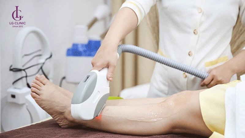 Người thực hiện liệu pháp laser trên chân tại một phòng khám, sử dụng thiết bị cầm tay chuyên dụng.