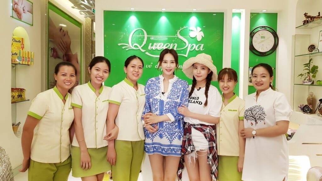 Nhóm người đứng trước biển hiệu spa màu xanh lá, mỉm cười và tạo dáng chụp ảnh.