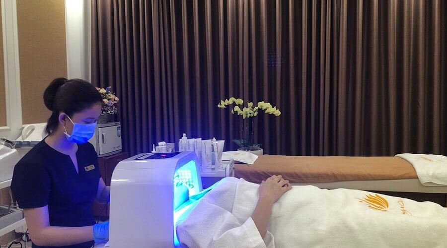 Người mặc đồng phục đang thực hiện liệu trình chăm sóc da mặt cho khách hàng trong phòng spa.