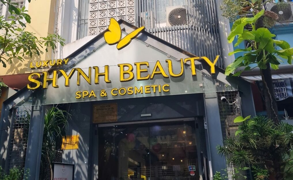 Mặt tiền cửa hàng spa và mỹ phẩm, biển hiệu lớn màu vàng, có cây xanh trang trí xung quanh.