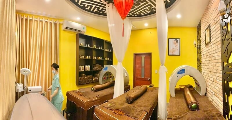 Phòng spa với giường massage, trang trí ấm cúng và trang thiết bị chăm sóc sức khỏe, có một người đang làm việc.