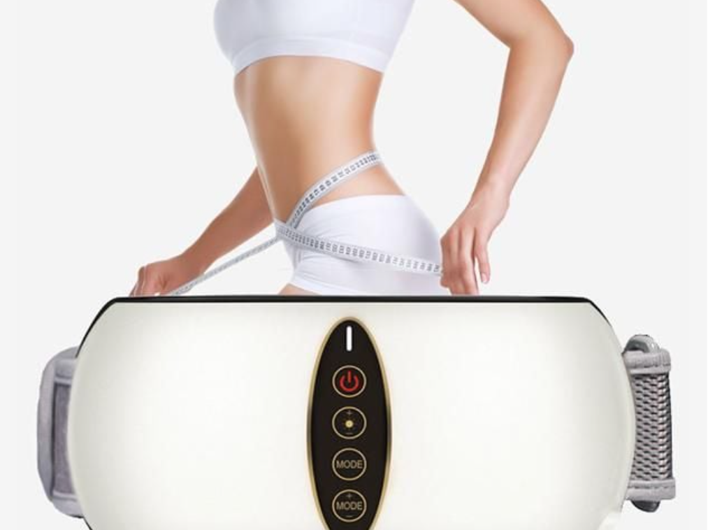 Người mặc đồ thể thao trắng, dùng thước dây đo vòng eo, bên cạnh là máy massage bụng màu trắng.