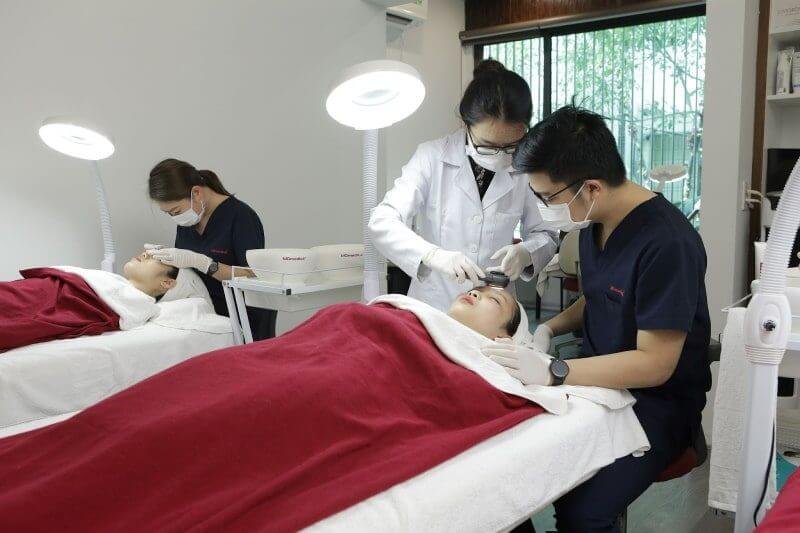 Nhân viên y tế thực hiện chăm sóc da cho khách hàng trong phòng thẩm mỹ, với ánh sáng từ đèn chuyên dụng.