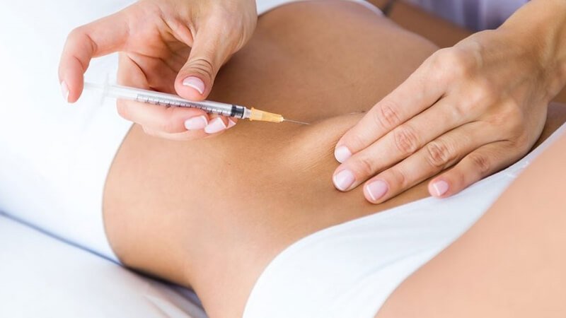 Người cầm kim tiêm chuẩn bị tiêm vào vùng bụng của một người khác trong bối cảnh y tế.