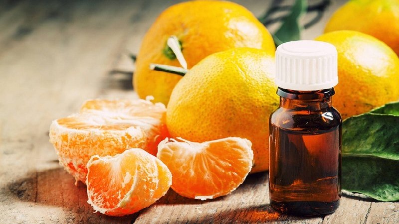 Chai tinh dầu màu nâu với nắp trắng cạnh quả cam và múi cam trên bàn gỗ.