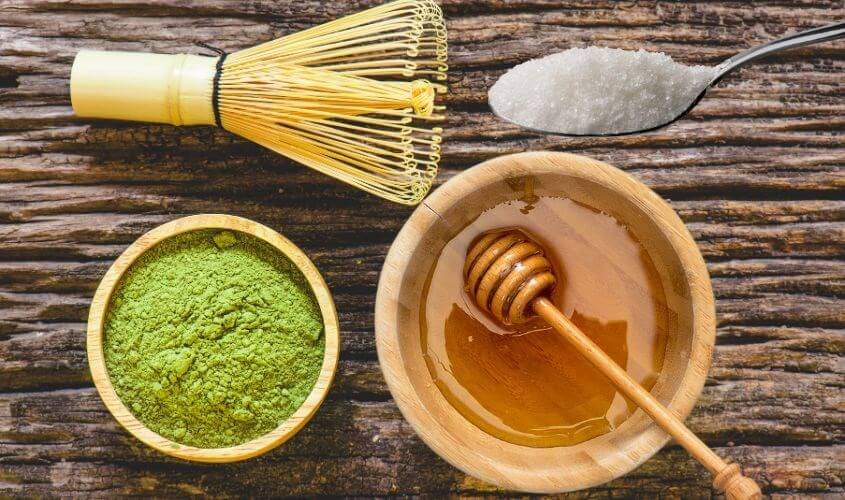 Bột matcha, mật ong, đường và chổi tre trên bề mặt gỗ.