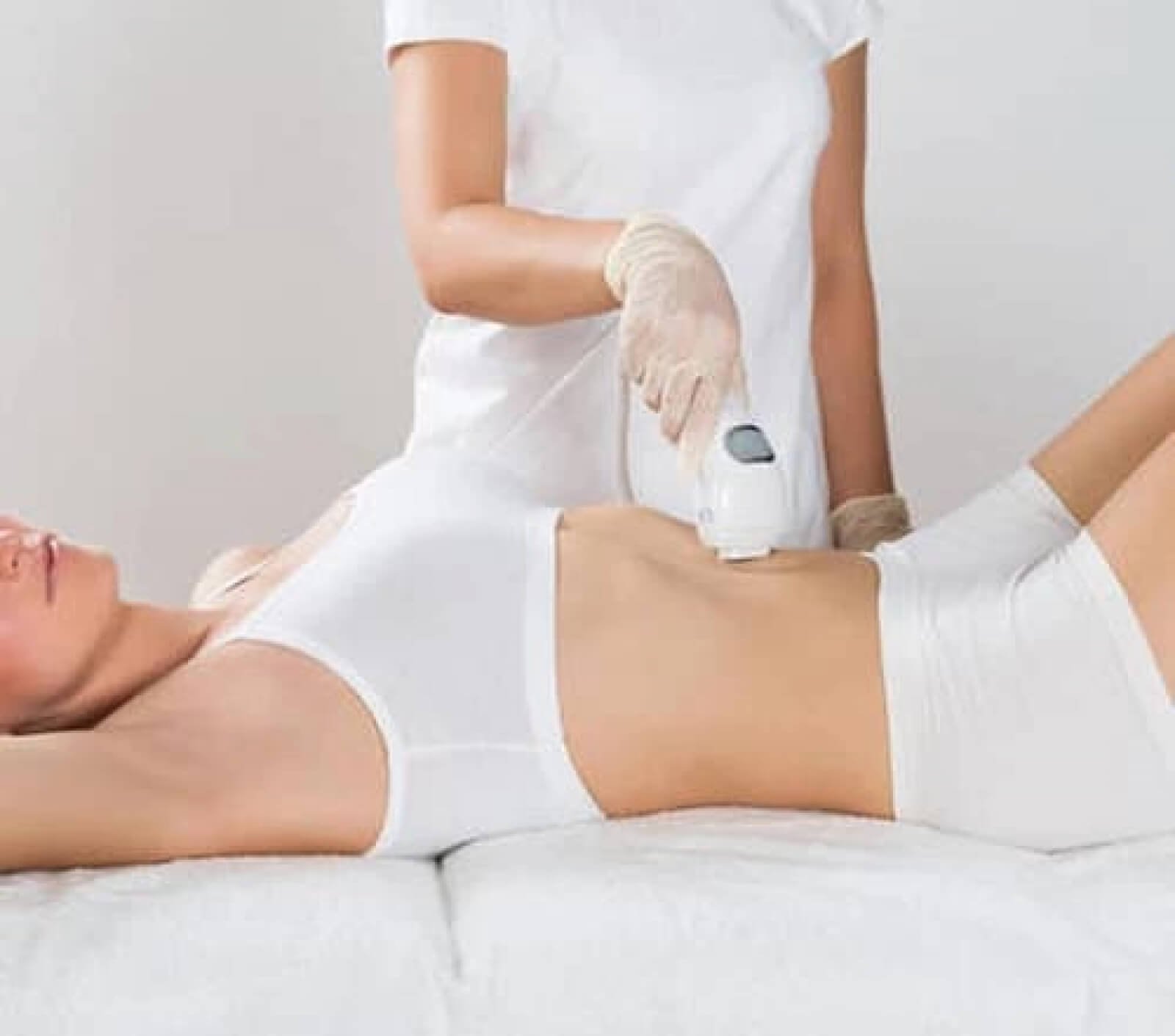 Nhân viên thực hiện liệu pháp làm đẹp bằng máy trên vùng bụng của khách hàng nằm trên giường.