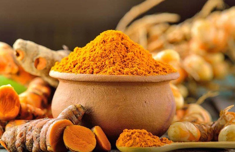 Bột màu vàng cam trong bát đất, xung quanh là củ tươi và lát cắt cùng màu.