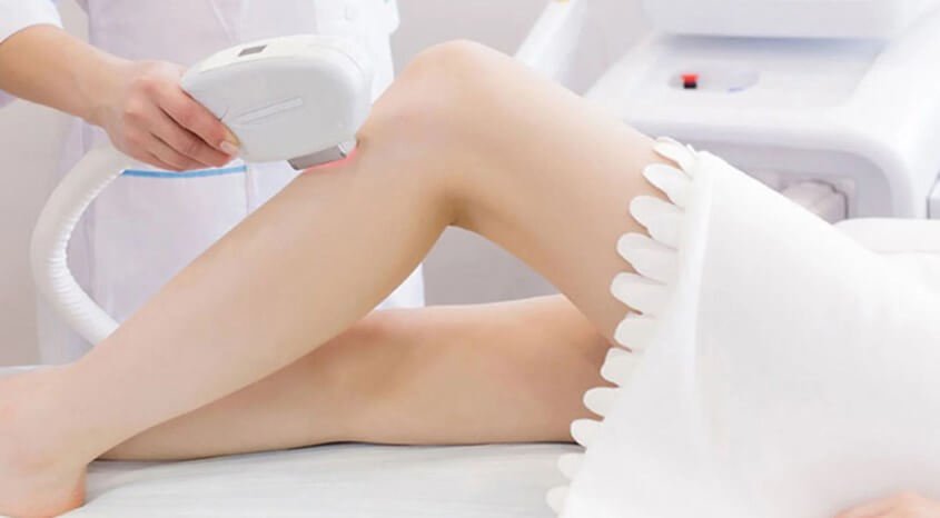 Người đang sử dụng thiết bị cầm tay điều trị trên chân của khách hàng trong phòng thẩm mỹ.