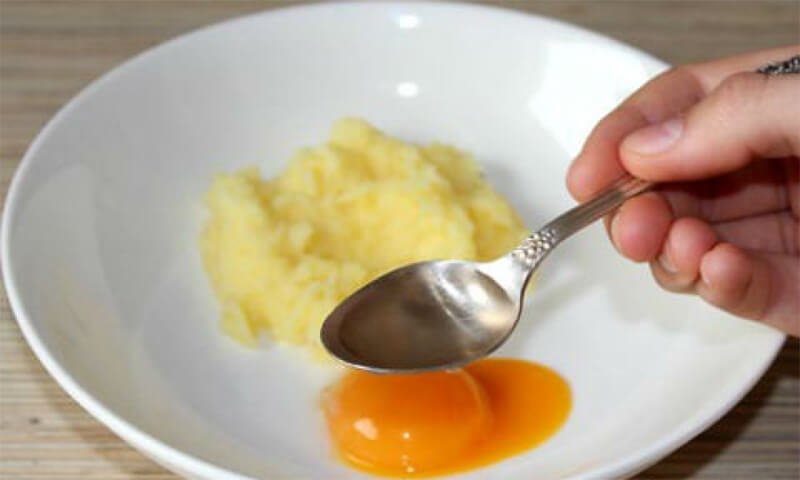 Một đĩa chứa khoai tây nghiền và lòng đỏ trứng, một tay cầm thìa trên bề mặt.