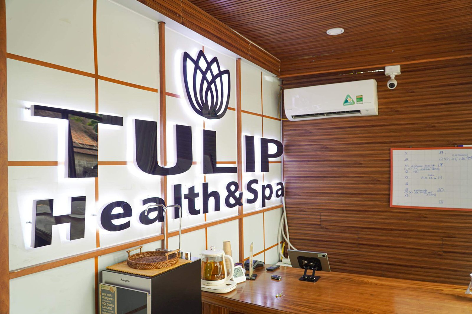 Bên trong một spa với bảng hiệu lớn, máy điều hòa trên tường và bàn tiếp tân có ấm đun nước.