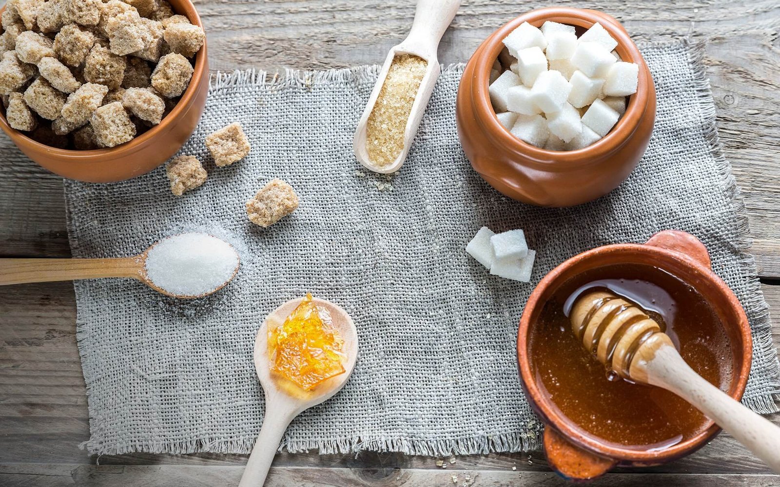 Các loại đường và mật ong trong bát, muỗng trên bàn gỗ, đặt trên khăn vải.