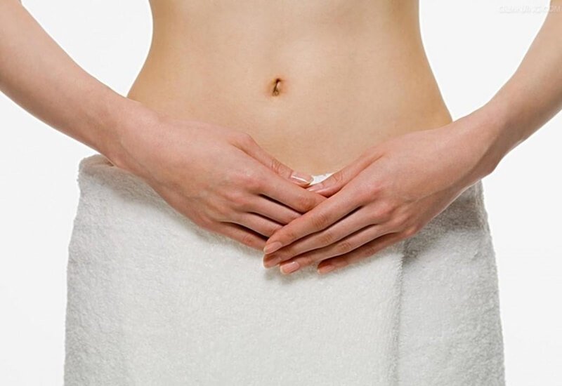 Người đứng với tay đặt trước bụng, quấn khăn trắng, nền trắng.