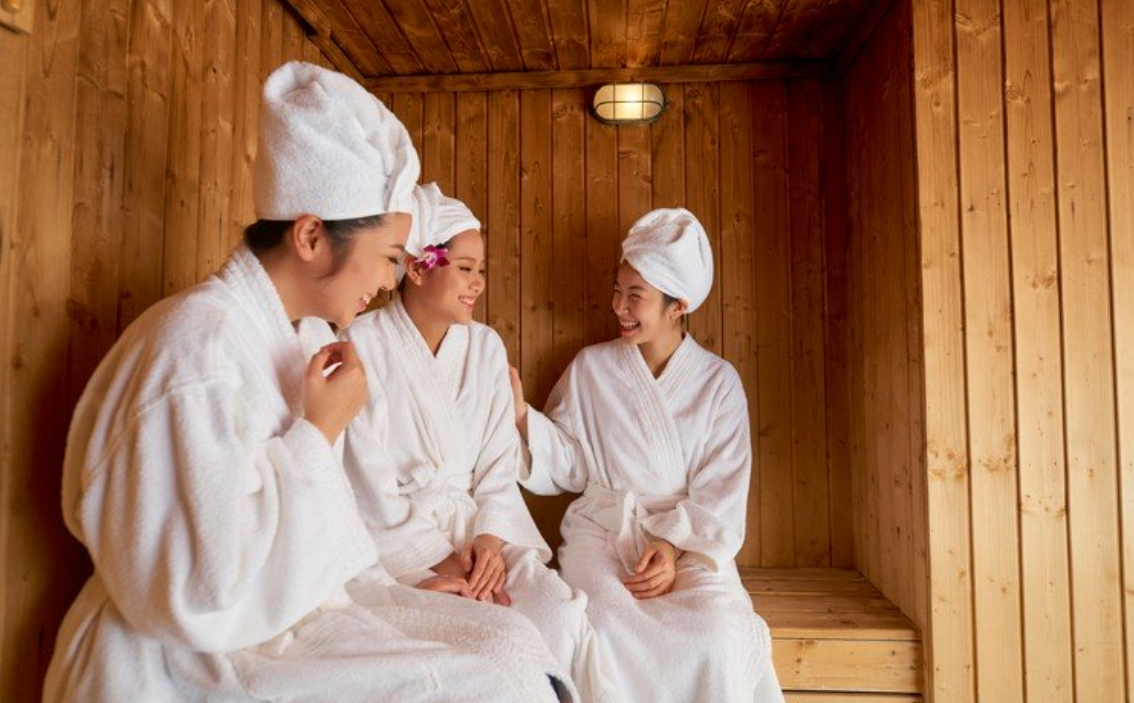 Ba người mặc áo choàng tắm trắng, đội khăn, ngồi trò chuyện trong phòng xông hơi gỗ.