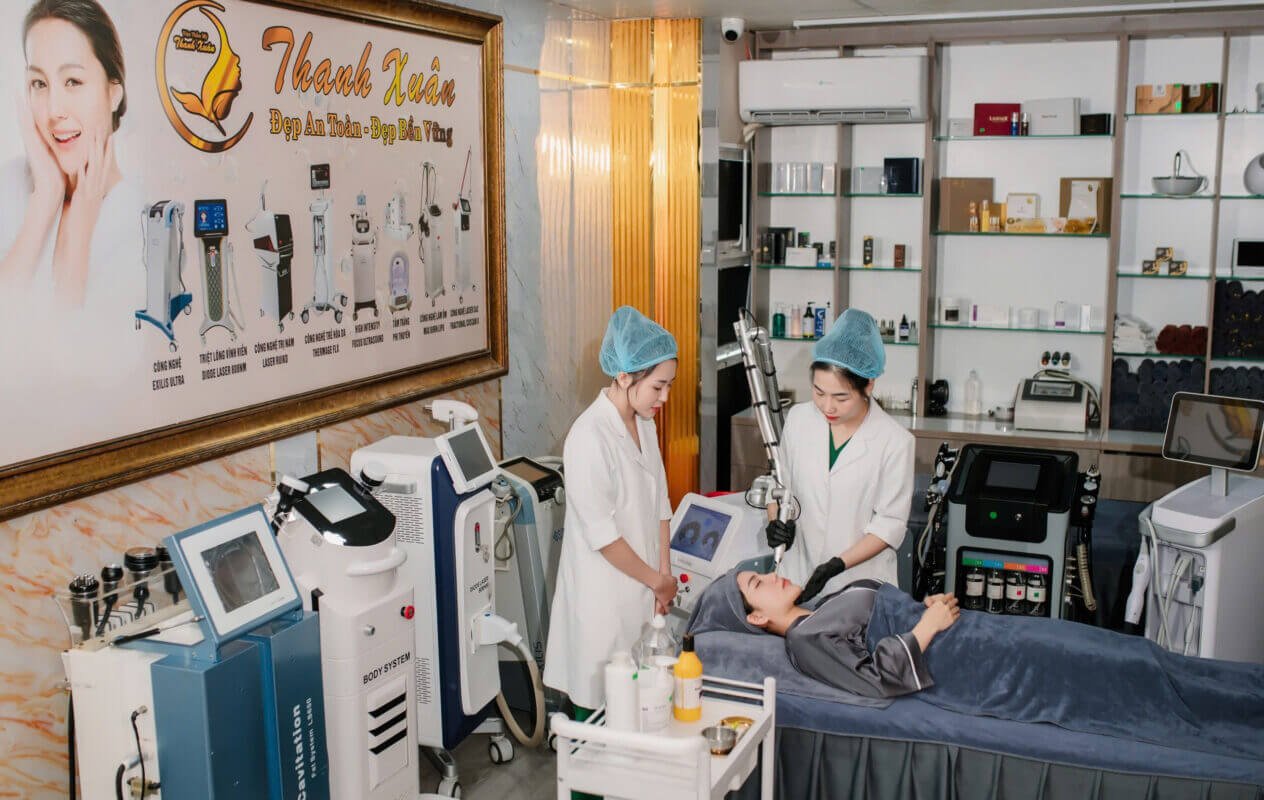 Nhân viên thẩm mỹ viện đang thực hiện liệu trình chăm sóc da cho khách hàng trong phòng trang bị máy móc hiện đại.
