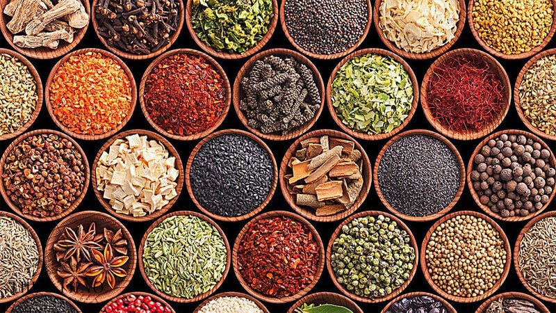 Các bát gỗ chứa nhiều loại gia vị và thảo mộc khác nhau, sắp xếp thành hàng và cột với màu sắc đa dạng.