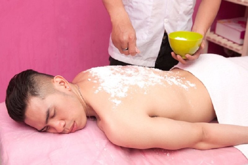 Người đang nằm thư giãn với sản phẩm chăm sóc da được thoa lên lưng trong một không gian màu hồng.