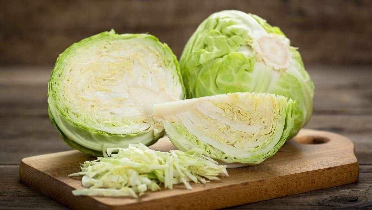 Bắp cải tươi được cắt lát và bào nhỏ trên thớt gỗ, nền gỗ tối màu.
