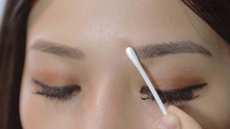 Người đang dùng tăm bông làm sạch hoặc chỉnh sửa vùng lông mày gần mắt.