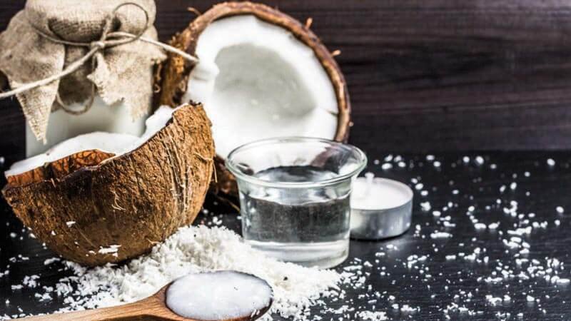 Nửa trái dừa, sữa dừa trong ly, và dừa nạo trên nền gỗ tối, cạnh nến nhỏ.
