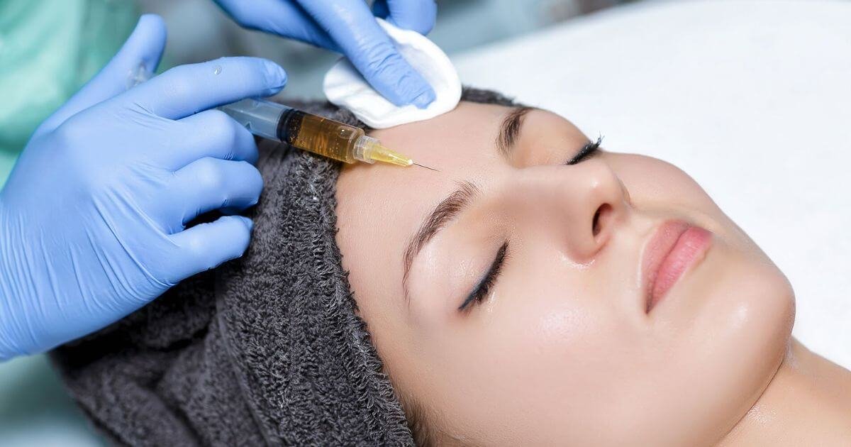 Người được tiêm chất lỏng vào trán bởi một người đeo găng tay xanh.
