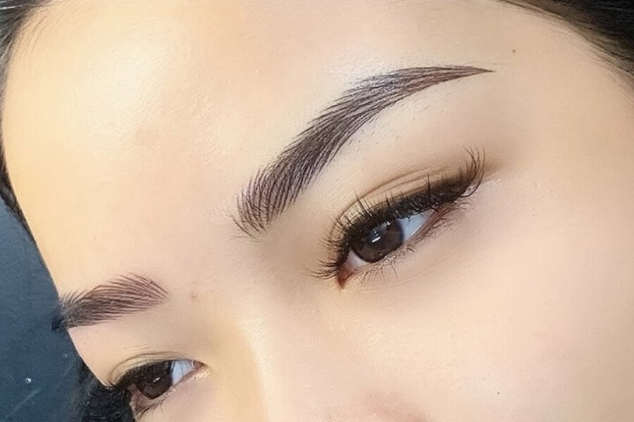 Cận cảnh đôi mắt với hàng lông mày đậm và lông mi dài, nền da mịn màng, ánh sáng tự nhiên.