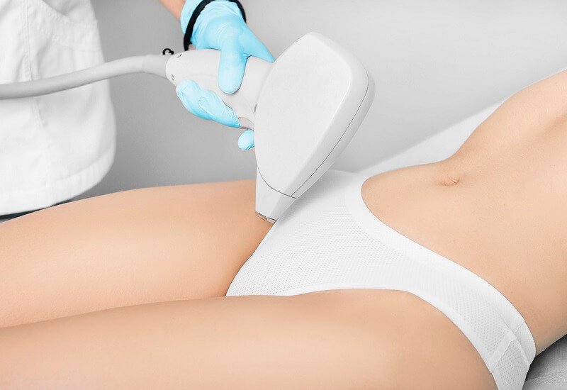 Người đeo găng tay xanh sử dụng thiết bị chiếu tia laser lên vùng da bụng của một người đang nằm.