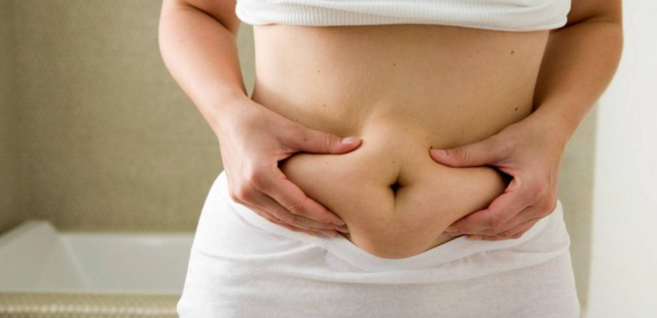 Người đang nắm phần da bụng của mình bằng hai tay, mặc áo ngắn và quần trắng.