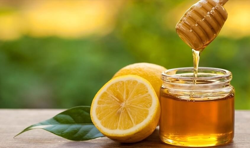 Chanh tươi và mật ong trong lọ thủy tinh trên bàn gỗ, nền xanh mờ.