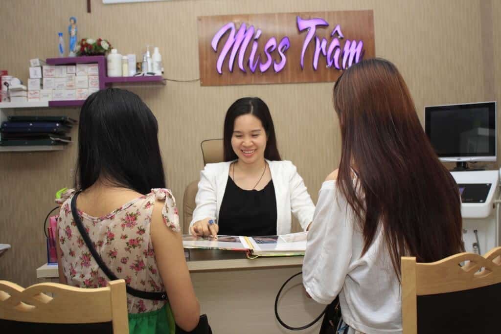 Một người phụ nữ ngồi bàn làm việc, trao đổi với hai người đối diện trong không gian văn phòng trang trí ấm cúng.