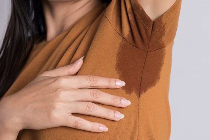 Áo nâu với vết ướt lớn dưới cánh tay, người mặc chạm tay vào khu vực đó.