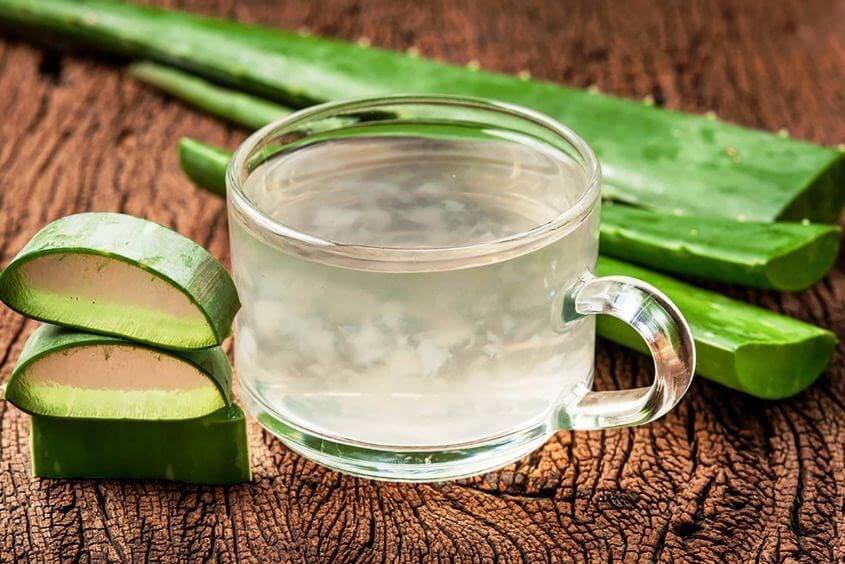 Cốc nước nha đam tươi mát bên cạnh các lát nha đam trên bề mặt gỗ nâu.