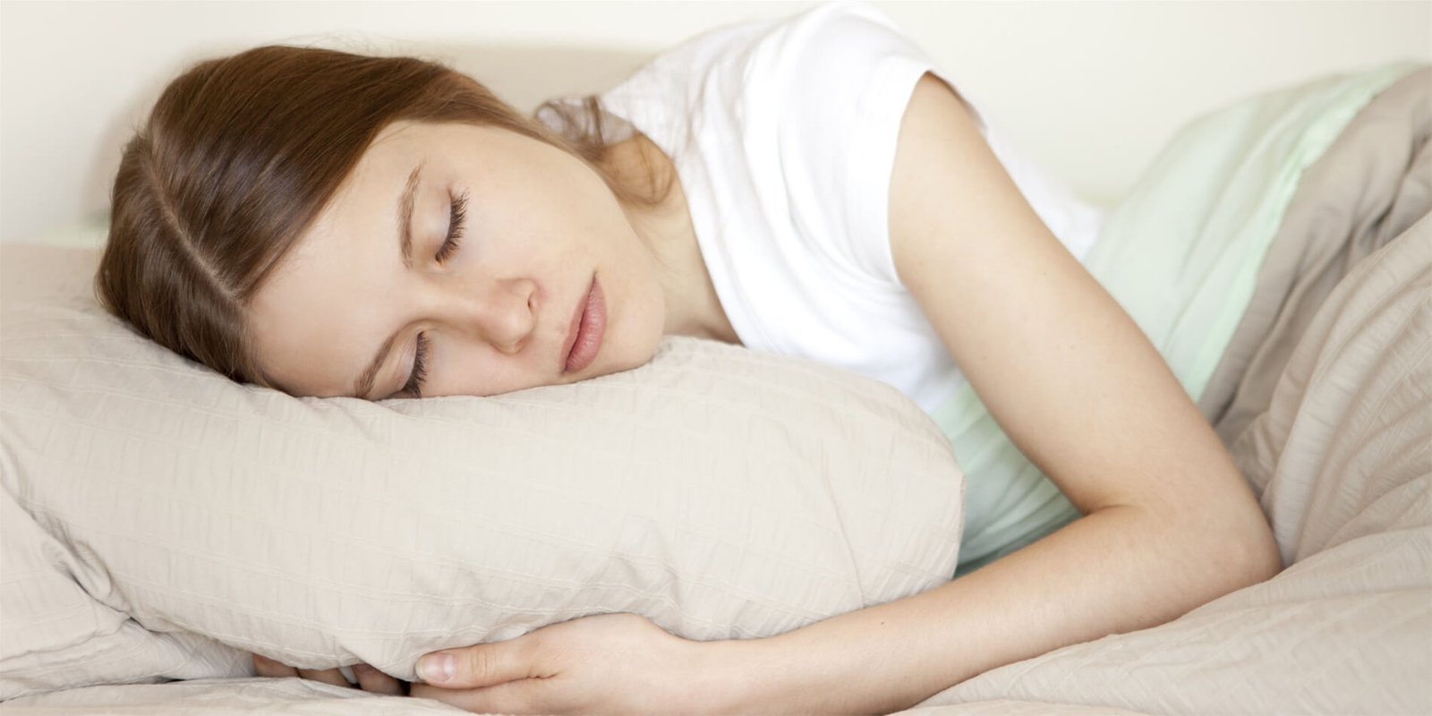 Người nằm ngủ trên giường, đầu gối lên gối màu be, với chăn phủ nhẹ nhàng.