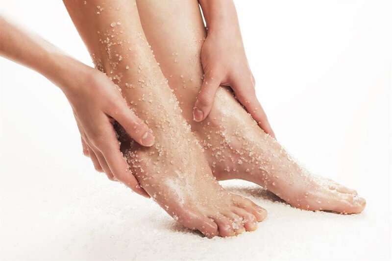 Hai bàn chân được chà muối tẩy tế bào chết, đôi tay nhẹ nhàng xoa bóp trên nền trắng.