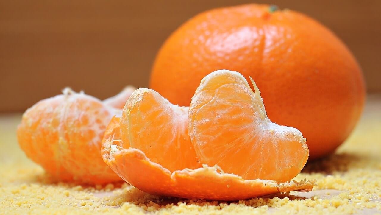 Quả cam bóc vỏ, một vài múi cam tươi được đặt trên nền màu cam nhạt.