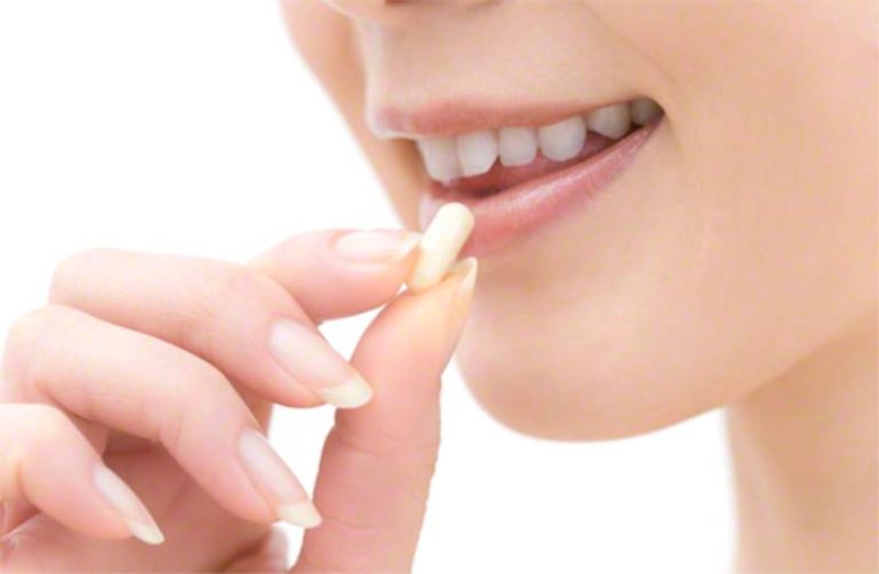 Người đang cầm một viên thuốc gần miệng, với nụ cười nhẹ, trên nền trắng.