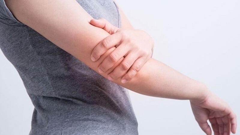 Người mặc áo xám đang cầm khuỷu tay bằng tay kia, có thể biểu hiện đau hoặc khó chịu.