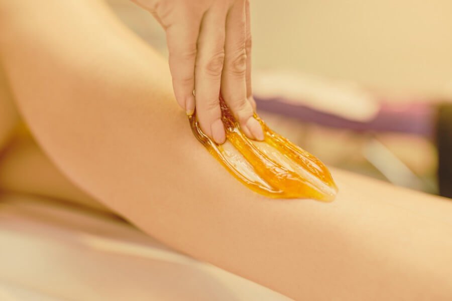Tay đang áp dụng sáp màu vàng lên da chân, có thể là cho mục đích tẩy lông hoặc chăm sóc da.