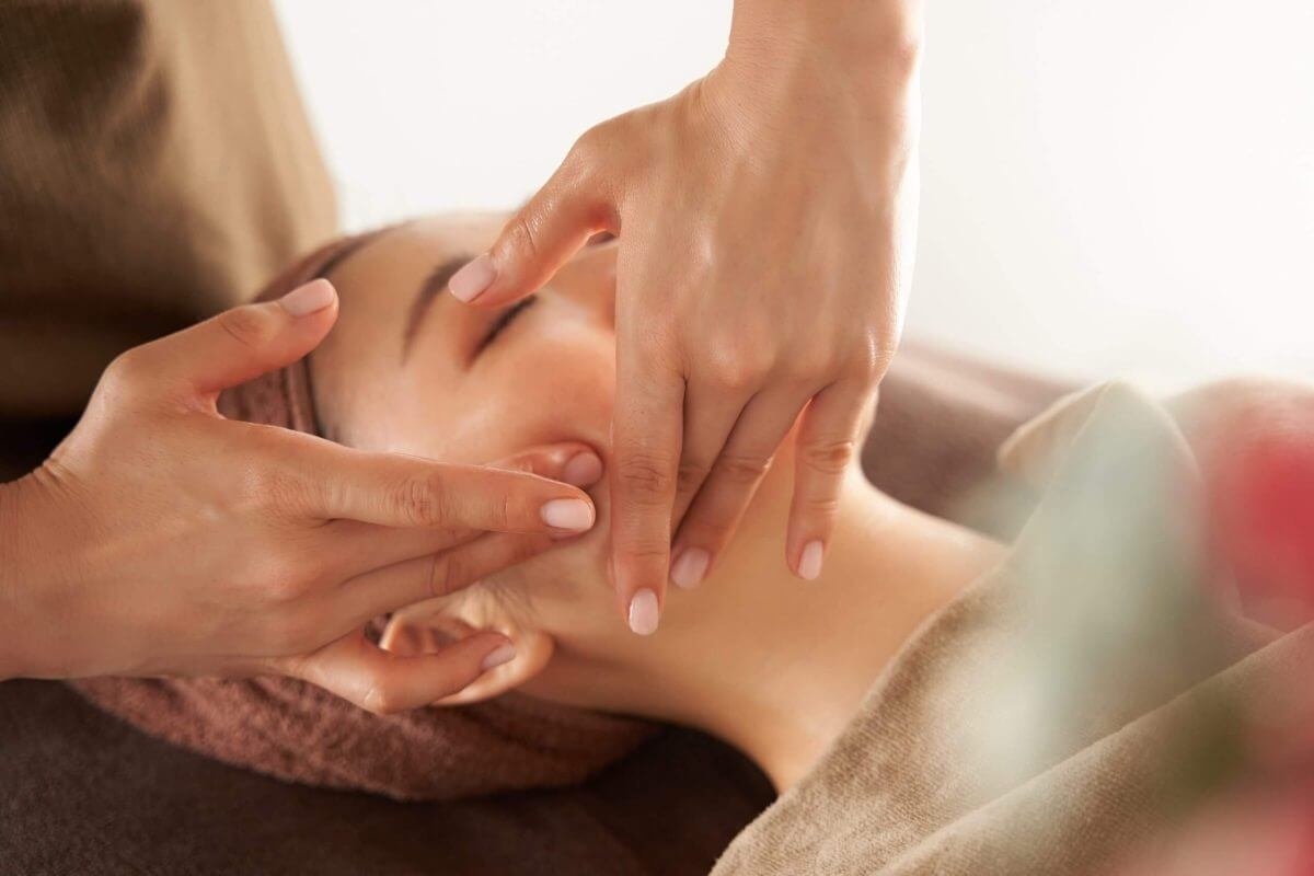 Người đang được mát-xa mặt thư giãn, tay mát-xa áp dụng kỹ thuật nhẹ nhàng lên gương mặt.