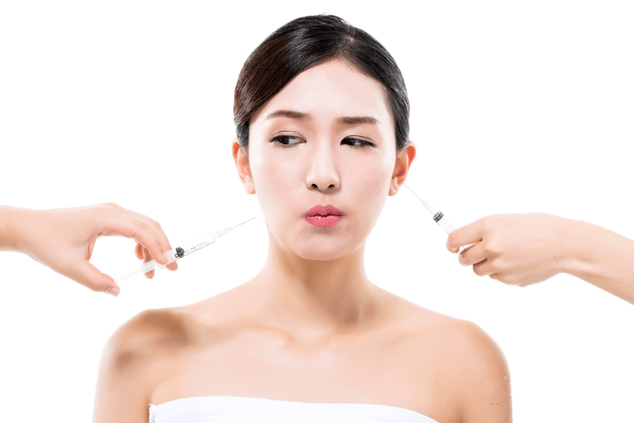 Người phụ nữ với hai ống tiêm ở hai bên mặt, biểu cảm chăm chú, nền trắng.