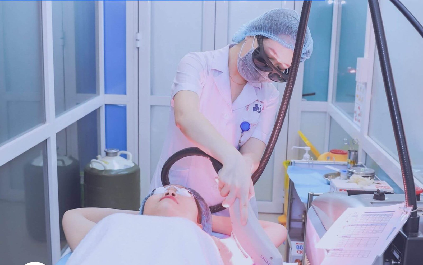Người trong trang phục y tế đang thực hiện liệu pháp laser cho một khách hàng nằm trên giường tại phòng chăm sóc da.