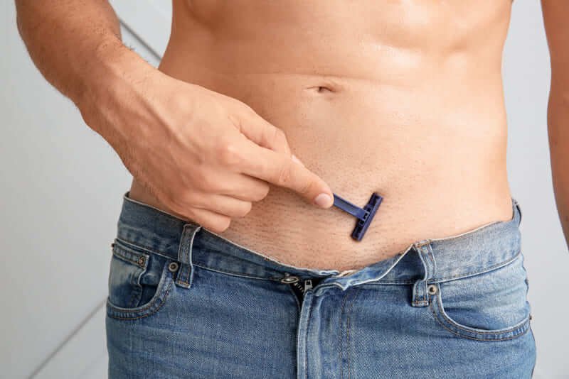 Người đang cạo lông bụng bằng dao cạo màu xanh, mặc quần jeans xanh, phần bụng lộ ra.