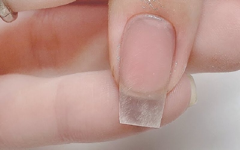 Cận cảnh móng tay được nối dài bằng miếng nhựa trong suốt, trên nền da tay tự nhiên.