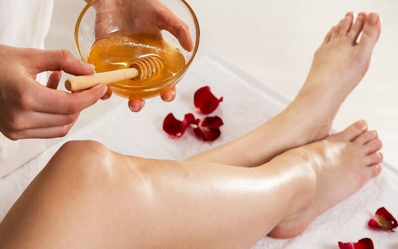 Người đang thoa mật ong lên chân, bên cạnh là các cánh hoa hồng đỏ trên khăn trắng.